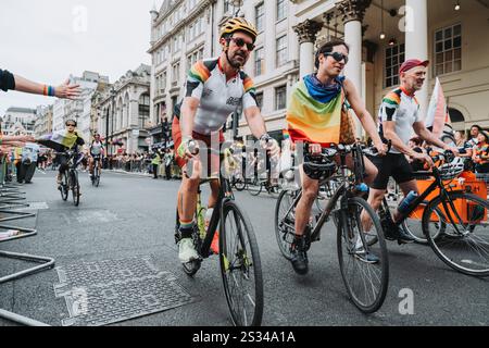 Un gioioso gruppo di ciclisti che sfoggiano bandiere e colori arcobaleno mentre partecipano a un Pride of London 2024 Foto Stock