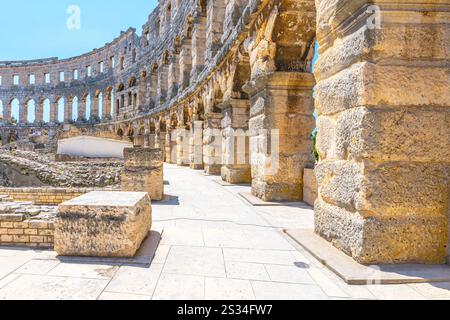 I visitatori passeggiano attraverso l'antico anfiteatro romano di Pola, la penisola istriana, la Croazia, ammirando la sua splendida architettura e il suo significato storico sotto un cielo azzurro. Foto Stock