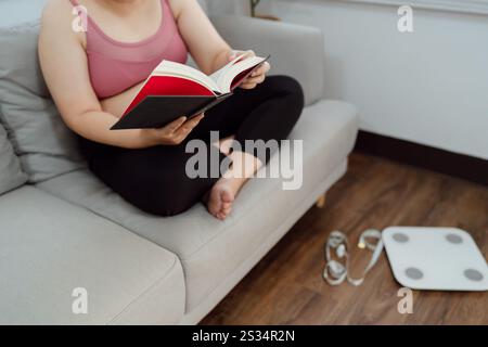 Donna in sovrappeso che legge un libro per perdere peso. Donna grassa preoccupata per la dieta del peso perdere stile di vita. Foto Stock