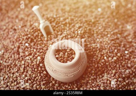 Immagine di sfondo di un gran mucchio di grano saraceno, al centro del quale si trova una piccola brocca e una spatola in legno per i cereali Foto Stock