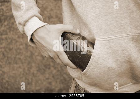 Il TRAFFICANTE DI DROGA Prendendo in borsa con cocaina al di fuori della tasca di felpa con cappuccio scuro su sfondo piastrelle close up. Il traffico di narcotici concetto. La tossicodipendenza Foto Stock