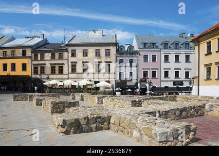 Fila di case storiche e panchine di pietra su una piazza soleggiata, fondazioni della chiesa parrocchiale di San Michele e case in via Grodzka, Lublino, Polonia, UE Foto Stock