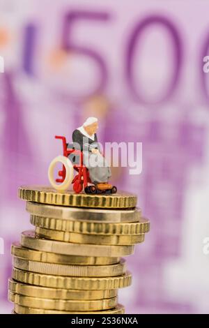 Donna in sedia a rotelle su mucchio di soldi, foto simbolica per la disabilità, indennità di assistenza e costi di assistenza sanitaria Foto Stock
