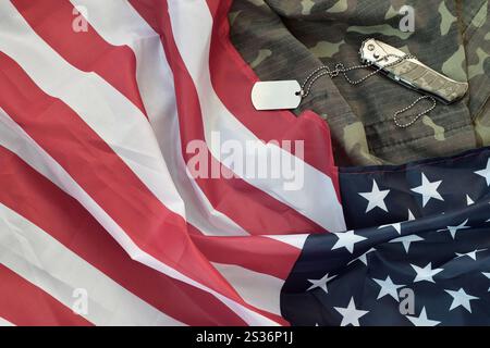 Gettone e coltello per il cane dell'esercito si trova sulla vecchia uniforme camouflage e sulla bandiera degli Stati Uniti piegata. Sfondo per il design Veterans Day Foto Stock