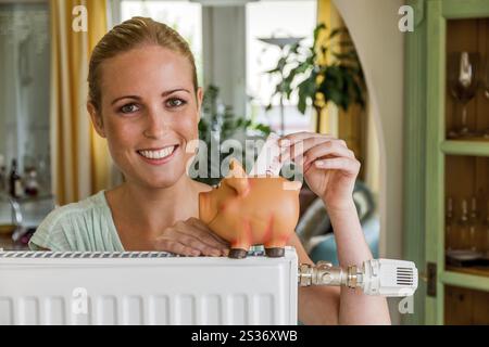Una giovane donna con un radiatore e un salvadanaio. Foto simbolica per risparmiare energia e riscaldare l'Austria Foto Stock
