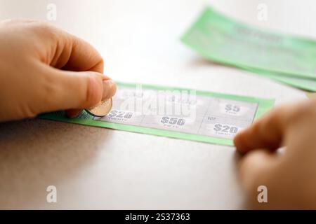 Vista ravvicinata della moneta d'argento in mano al giocatore che graffia la falsa carta della lotteria. Lotteria gioco d'azzardo concetto, gratta carte tipo di lotteria Foto Stock