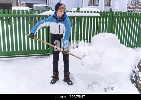 Un adolescente scaglia la nuova neve da un sentiero. Inizio dell'inverno in Austria Foto Stock