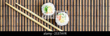 Rotoli di Sushi e bacchette di legno giacciono su una cannuccia di bambù serwing mat. Tradizionale cibo asiatico. Vista dall'alto. Piatto minimalismo laici shot con copia spazio. Foto Stock