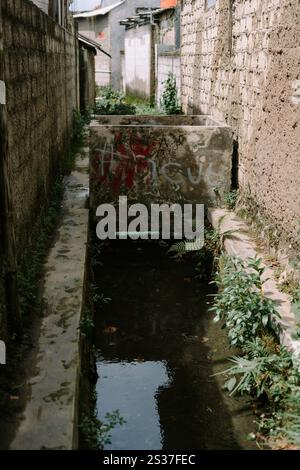 Un piccolo corso d'acqua scorre attraverso uno stretto vicolo, riflettendo gli edifici circostanti e il cielo. Foto Stock