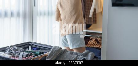 Ragazza asiatica che prepara le vacanze scegliendo i vestiti con guardaroba in camera da letto prima del viaggio delle vacanze. Foto Stock