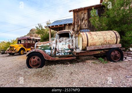 Un vecchio camion è parcheggiato davanti a una casa. Il carrello è ricoperto di ruggine e ha una parte superiore verde. La casa è fatta di legno e ha un tetto inclinato. La sc Foto Stock