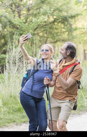 Coppia senior che si gode un gioioso selfie con il proprio smartphone mentre cammina attraverso un bellissimo parco di madrid, in spagna, circondato dalla natura Foto Stock