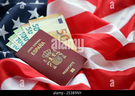 Passaporto spagnolo rosso dell'Unione europea e denaro sullo sfondo della bandiera nazionale degli Stati Uniti da vicino. Concetto di turismo e diplomazia. Spagnolo rosso Foto Stock