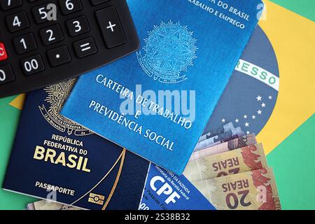 Passaporto del Brasile, carta dei contribuenti CPF e carta di lavoro con banconote brasiliane del Reais sullo sfondo della bandiera da vicino. Passaporto del Brasile, contribuente CPF Foto Stock