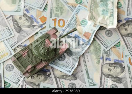 Carro armato su banconote da cento dollari schiacciate. Contesto del finanziamento di guerra e del prezzo di supporto militare per gli Stati Uniti d'America. Serbatoio su deformato Foto Stock