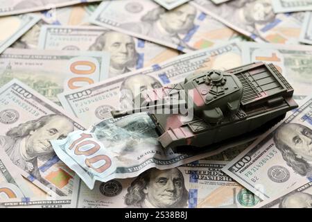 Carro armato su banconote da cento dollari schiacciate. Contesto del finanziamento di guerra e del prezzo di supporto militare per gli Stati Uniti d'America Foto Stock