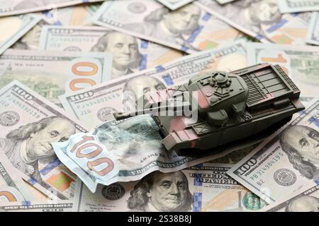 Carro armato su banconote da cento dollari schiacciate. Contesto del finanziamento di guerra e del prezzo di supporto militare per gli Stati Uniti d'America. Serbatoio su deformato Foto Stock