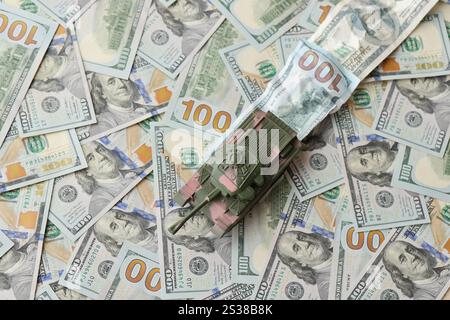 Carro armato su banconote da cento dollari schiacciate. Contesto del finanziamento di guerra e del prezzo di supporto militare per gli Stati Uniti d'America. Serbatoio su deformato Foto Stock