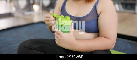 Obesa donna asiatica dieta perdita di peso in abbigliamento sportivo bere bevanda sana. Donna grassa asiatica sportiva che beve succo sano verde dopo il benessere dell'esercizio fisico Foto Stock