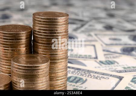 Crescono pile di monete ucraine in pile crescenti. Il denaro ucraino giace su banconote da cento dollari. Il denaro ucraino giace su molte centinaia di dollari Foto Stock