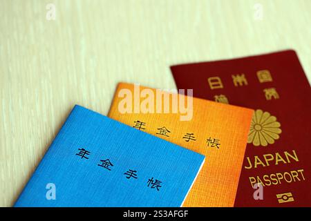 Opuscoli di assicurazione pensionistica giapponese sul tavolo con passaporto. Libro blu e arancione delle pensioni per i pensionati giapponesi da vicino. Assicurazione pensionistica giapponese Foto Stock