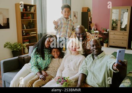 Scatto ad angolo alto di un uomo afroamericano che scatta selfie con la sua amata moglie caucasica e i figli con i nipoti in salotto Foto Stock
