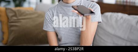 Donna asiatica che utilizza l'assistente vocale sullo smartphone a casa conversazione con assistente online chat vocale bot conversazionale ai tecnologie moderne Foto Stock