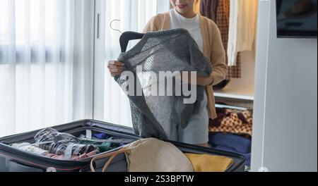 Ragazza asiatica che prepara le vacanze scegliendo i vestiti con guardaroba in camera da letto prima del viaggio delle vacanze. Foto Stock