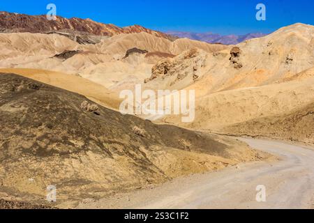 Una strada si snoda attraverso un paesaggio desertico. La strada è sporca e il cielo è blu. Il deserto è arido e roccioso Foto Stock