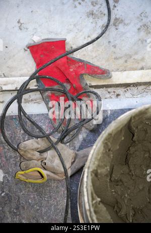 i guanti da lavoro sono posati sul pavimento e il cemento nel secchio durante i lavori di ristrutturazione della casa Foto Stock