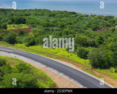 Strada asfaltata sullo sfondo verde della giungla accanto alla vista aerea con drone sullo sfondo dell'oceano Foto Stock