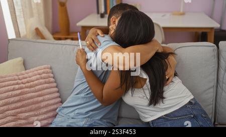 Coppia che celebra il test di gravidanza positivo abbracciando sul divano del soggiorno, ambiente interno che mette in evidenza la loro felicità e amore in un ambiente accogliente Foto Stock