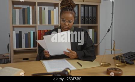 Giudice donna che legge documenti alla scrivania in ufficio con scaffali e bilance sullo sfondo. Foto Stock