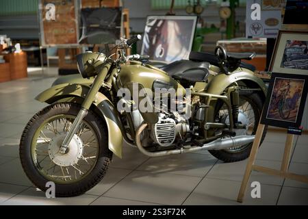 Motocicletta retrò di colore paludoso parcheggiata in un museo d'arte tra dipinti Foto Stock