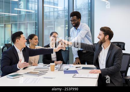 Team aziendale diversificato di successo che si uniscono con gioia, dando cinque. Team di finanziatori e investitori in tute aziendali che celebrano risultati di successo sul posto di lavoro. Foto Stock