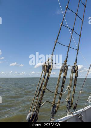 Ammira il mare con il cielo blu e le nuvole bianche viste attraverso le ringhiere e le corde tese di una nave a vela. Foto Stock