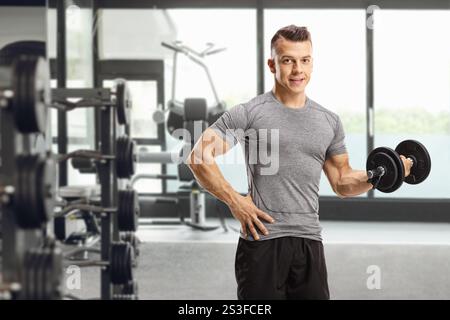 Giovane che fa esercizio con un manubrio e posa in palestra Foto Stock