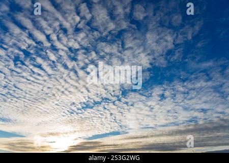 Le soffici nuvole si estendono sul cielo durante il tramonto, creando un'incredibile esposizione di colori mentre il sole tramonta all'orizzonte. La scena pacifica evocava Foto Stock