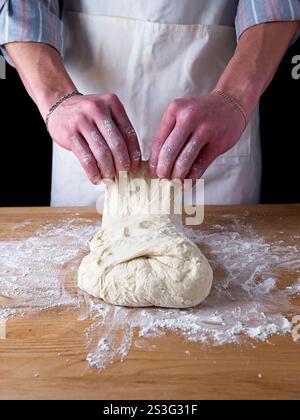 Il fornaio piega e impasta una palla di impasto su un tavolo. Foto Stock