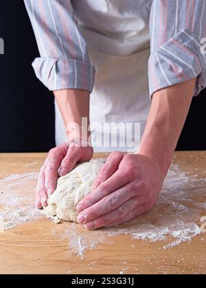 Una foto ravvicinata delle mani di un uomo che forma l'impasto in una palla su un tavolo di legno. Foto Stock