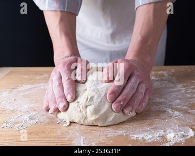 Una foto ravvicinata delle mani di un uomo che forma l'impasto in una palla su un tavolo di legno. Foto Stock