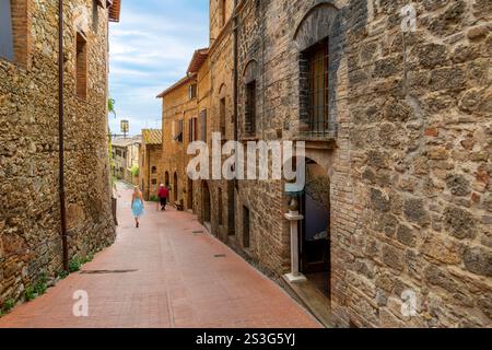 Una giovane donna cammina vicino a una donna anziana in uno stretto vicolo nel centro storico della collina di San Gimignano, in Italia, nella campagna toscana. Foto Stock