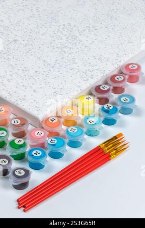 Un kit dettagliato di numeri per la verniciatura che include una tela numerata, contenitori di vernice multipli e pennelli con manico rosso. Divertimento creativo. Foto Stock