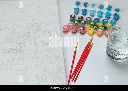 Kit di pittura per numeri con vasi, pennelli, tela e un bicchiere d'acqua su sfondo bianco. Divertimento creativo. Foto Stock