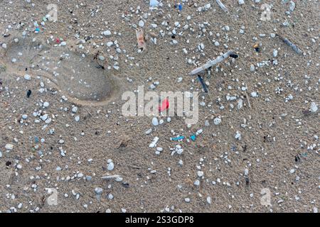 Spiaggia sabbiosa contaminata da microplastiche. Vista ravvicinata di microplastiche e rifiuti su una spiaggia. Impronte di una scarpa. Foto Stock