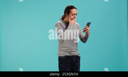 Uomo che ha un telefono cellulare, sta navigando sul sito di scommesse, festeggia dopo aver vinto soldi, isolato sullo sfondo dello studio. Persona allegra che si sente felice mentre scorri sullo smartphone, fotocamera A. Foto Stock