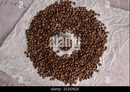 Vista dall'alto chicchi di caffè freschi aromatici in un piccolo bicchiere, chicchi di caffè circondati da uno sfondo chiaro. Miscela arabica e robusta Foto Stock