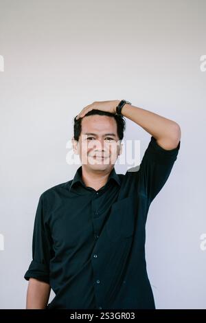 Un giovane allegro con una camicia nera che ride gioiosamente su un semplice sfondo bianco, catturando un momento schietto e spensierato. Foto Stock