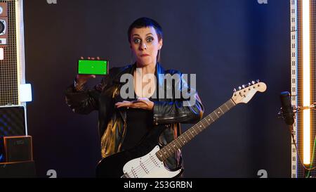La rock star ribelle e cool esegue una performance dal vivo puntando allo schermo dello spazio al nightclub, sentendosi potente nella sua giacca di pelle e nel trucco scuro. Ragazza potente e alla moda che si esibisce. Telecamera A.. Foto Stock