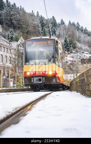Vista frontale di un tram su binari innevati, circondato da alberi ed edifici, Bad Wildbad, Foresta Nera, Germania, Europa Foto Stock